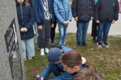 Uczniowie zapalają znicz i składają kwiaty pod pomnikiem