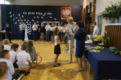 Uczennica klasy 1 odbierająca z rąk pani dyrektor i wychowawcy świadectwo.